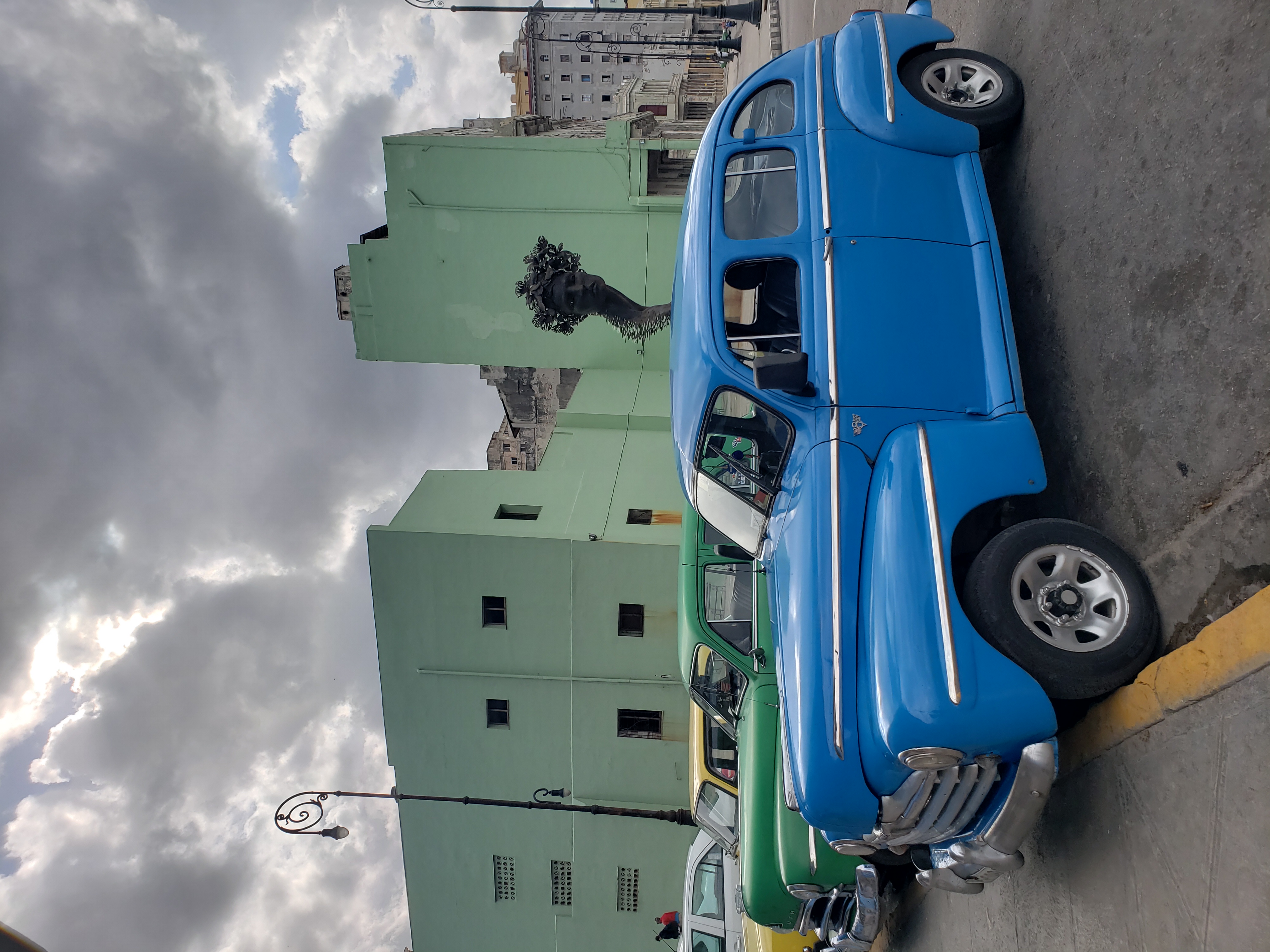 What lies beyond the classic cars? 3 classic cars in a row - blue, green, yellow. In Havana.