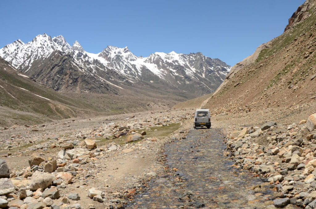 A car on the rough roads of Kaza-Manali route, with views of snow-capped Himalayan mountains. Kinnaur and Spiti road trip.