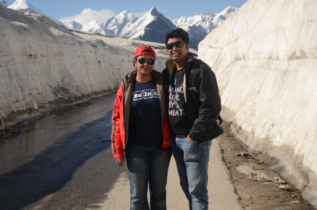 The two of us at the Rohtang Pass. Road covered with thick sheets of ice on either side of the road. Snow white mountains in the background. Kinnaur and Spiti road trip.