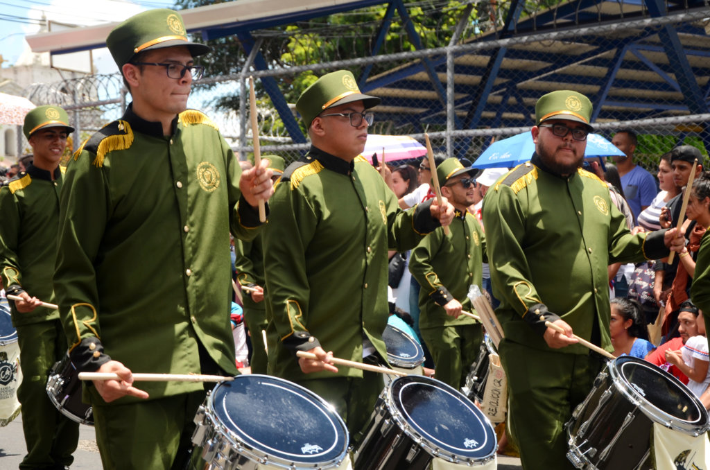 Three adult men beating drums, part of Independence Day celebrations in Heredia.