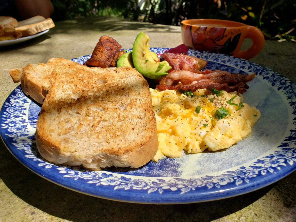 A plate of American breakfast at Cafe Rico, Puerto Viejo - it consists of two scrambled eggs, two bread toasts, bacon, avocado and tomato
