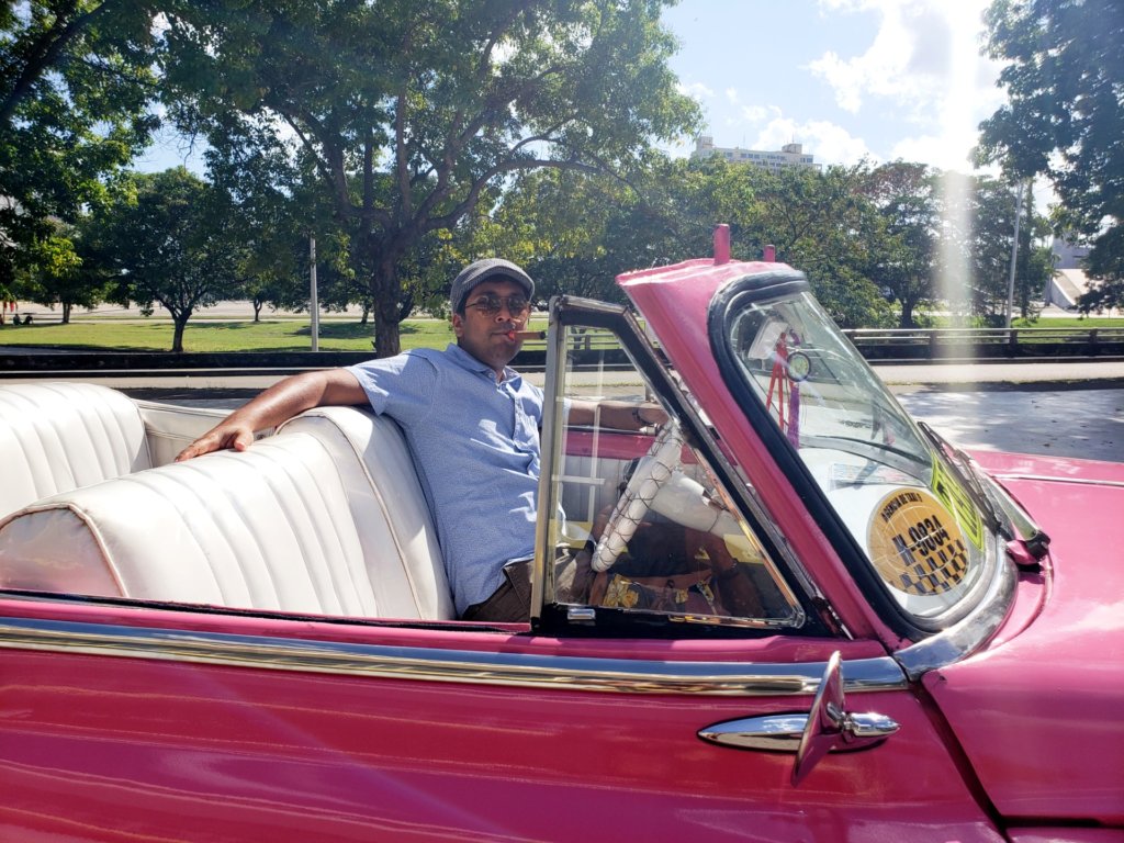 Indranil, posing behind the wheels, in a pink vintage car 