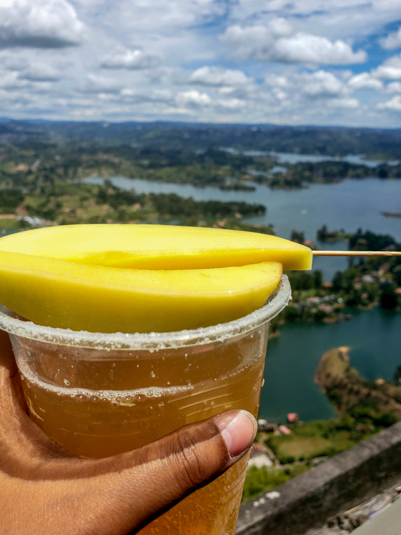 Mango michelada topped with a slice of mango. Lake view in the background.