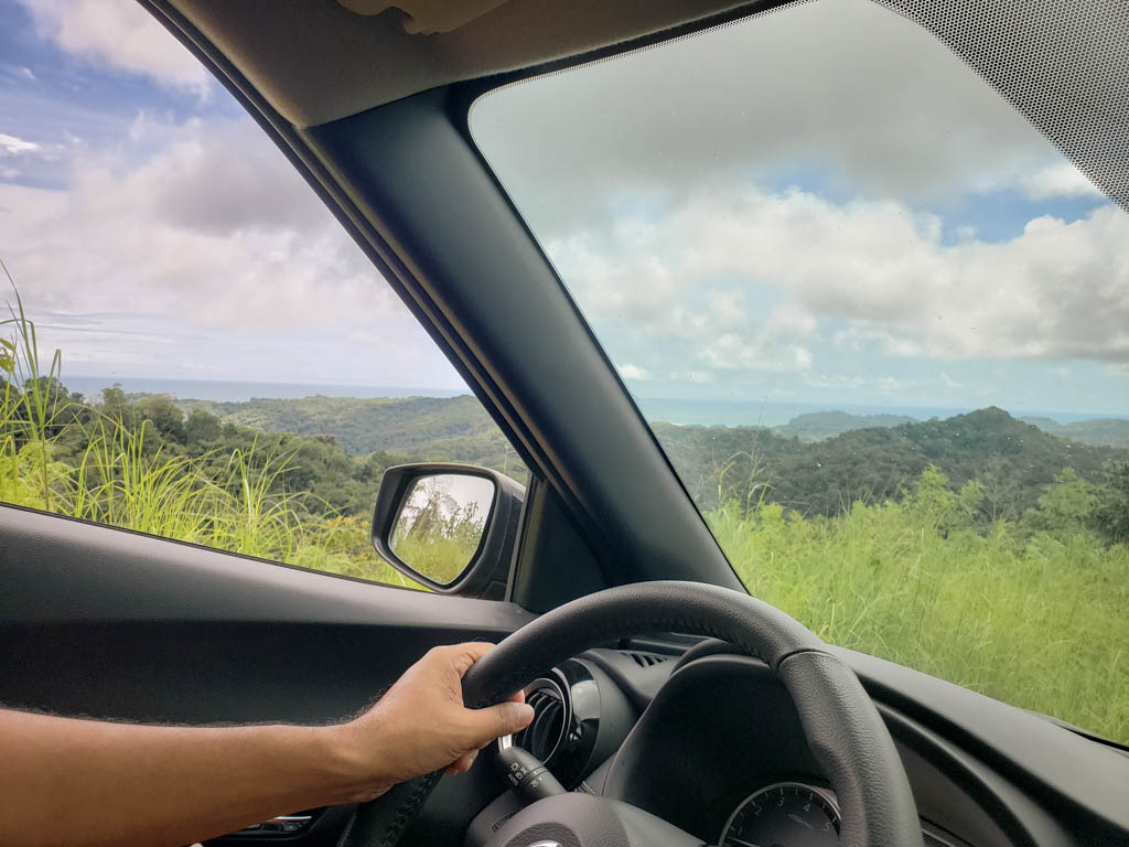 View of green fields and blue ocean from inside a car.