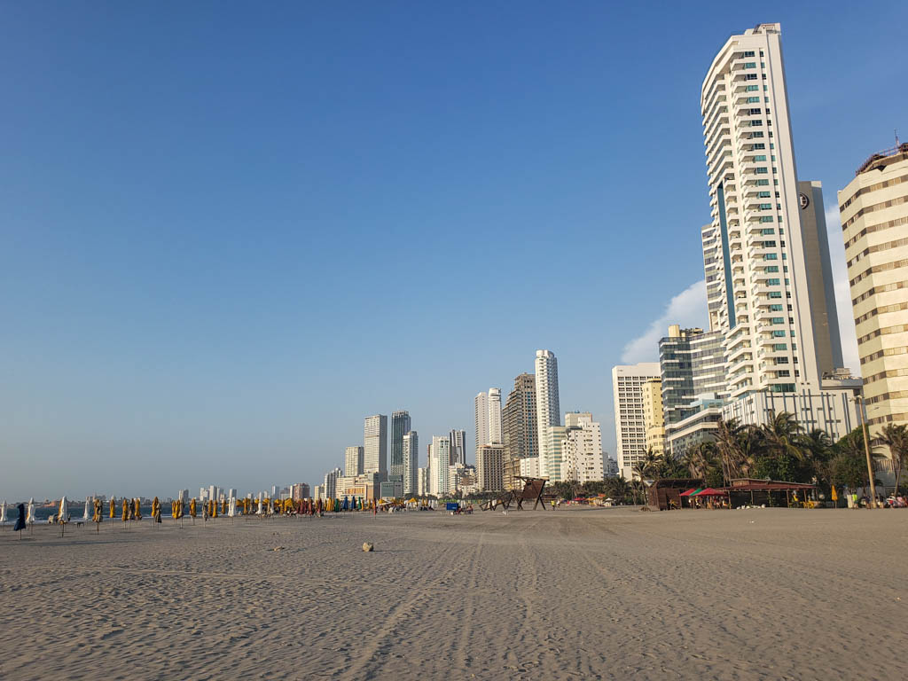 Long stretch of dark sand beach, lined by high-rise buildings at Bocagrande Beach in Cartagena.
