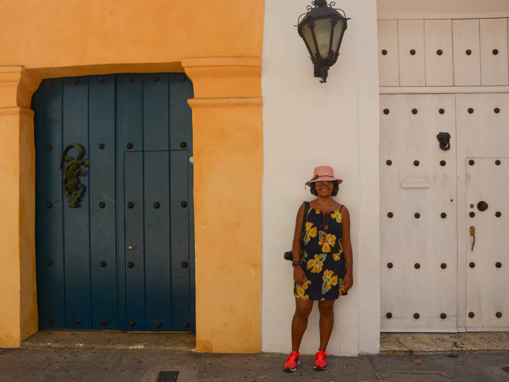 Pubali, standing next to the famously designed doors of Cartagena. Blue door against yellow wall and white door against white wall.