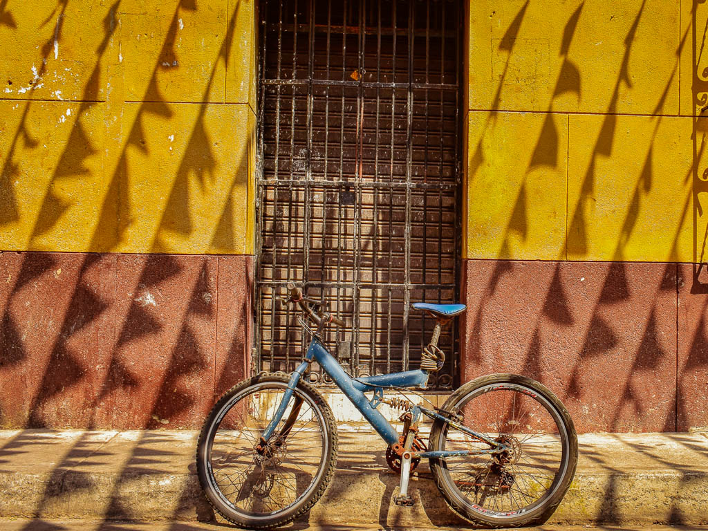 A blue bicycle parked against a colorful red and yellow wall, with brown door. Trinidad Square in Cartagena.