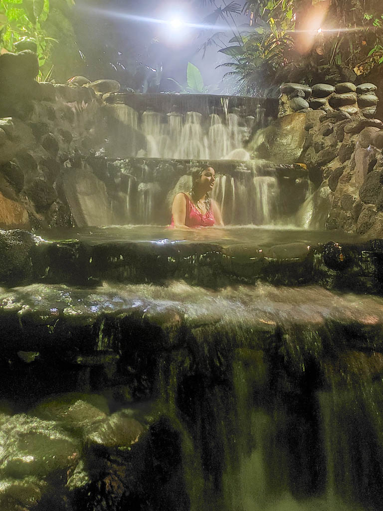 A woman sitting under the waterfall at one of the hot spring pools at Eco Termales in La Fortuna.