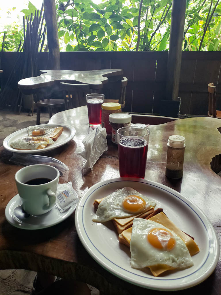 Breakfast of black cofee, jugo de Jamaica, breads, cheese and eggs, laid out on a wooden table.