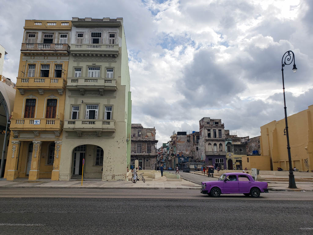 A purple colored car parked on the road, next to the street light post. On the left side, an old building standing tall. A typical sight in Havana, Cuba.