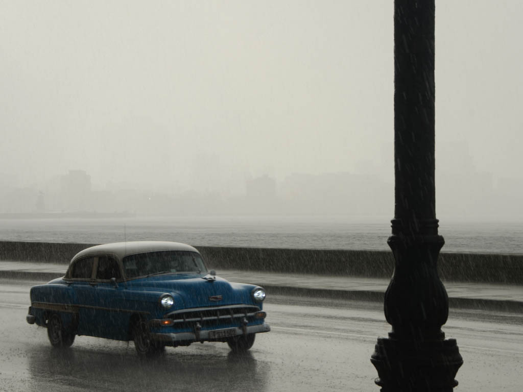 A blue and grey vintage car on the street next to Malecon, on a rainy day in Havana, Cuba.