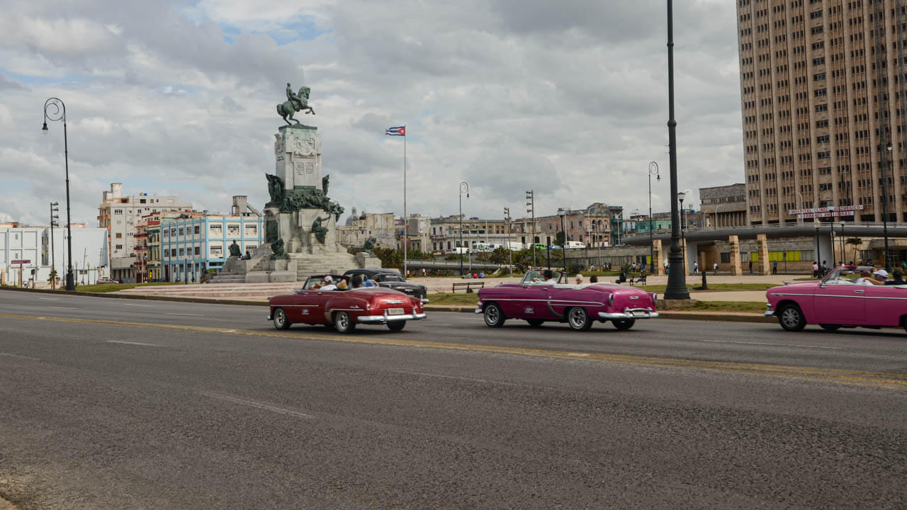 Street view of Havana, Cuba - 3 pastel colored classic cars on the road.
