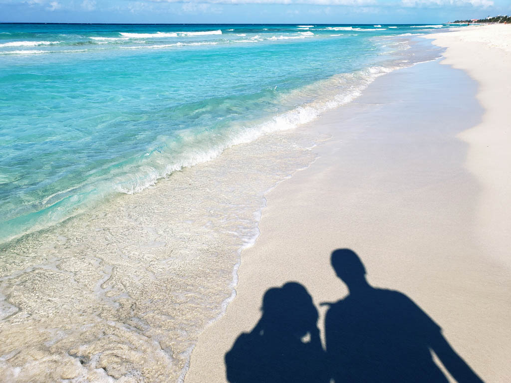 The shadow of a man and a woman on the white sand beach of Varadero in Cuba. The ocean water is clear blue. Varadero, a beach destination makes your Cuba 10 days itinerary complete