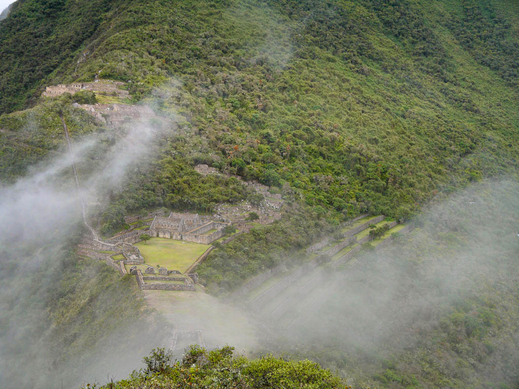View during Choquequirao Trek - Incan ruins amidst green mountains covered in white clouds.