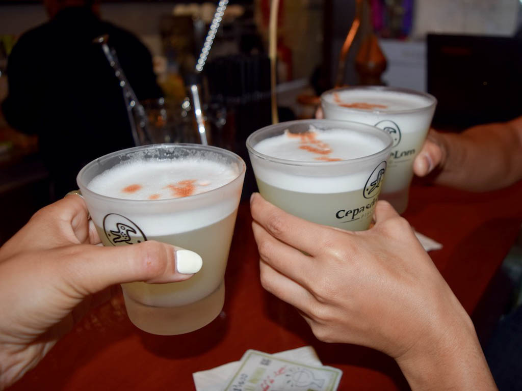 Three glasses of Pisco Sour being raised to a 'Cheers', at Pisco Sour museum.