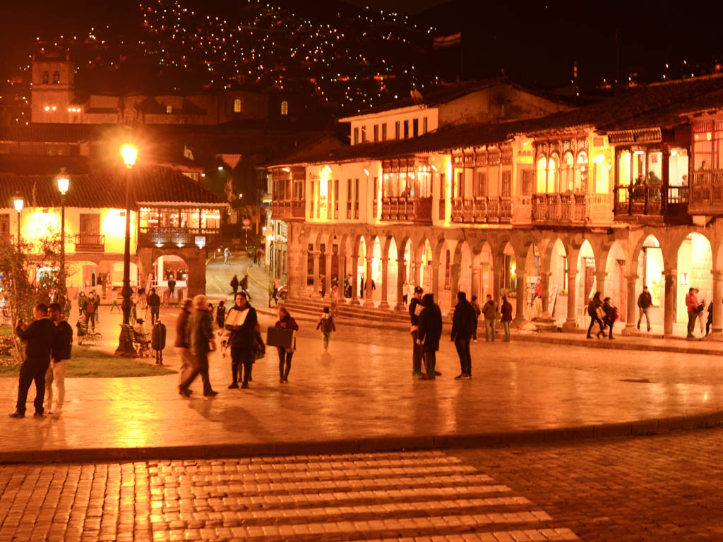 The golden glow of Plaza de Armas at night. Lot of people carrying on with their daily life in Cusco, Peru.