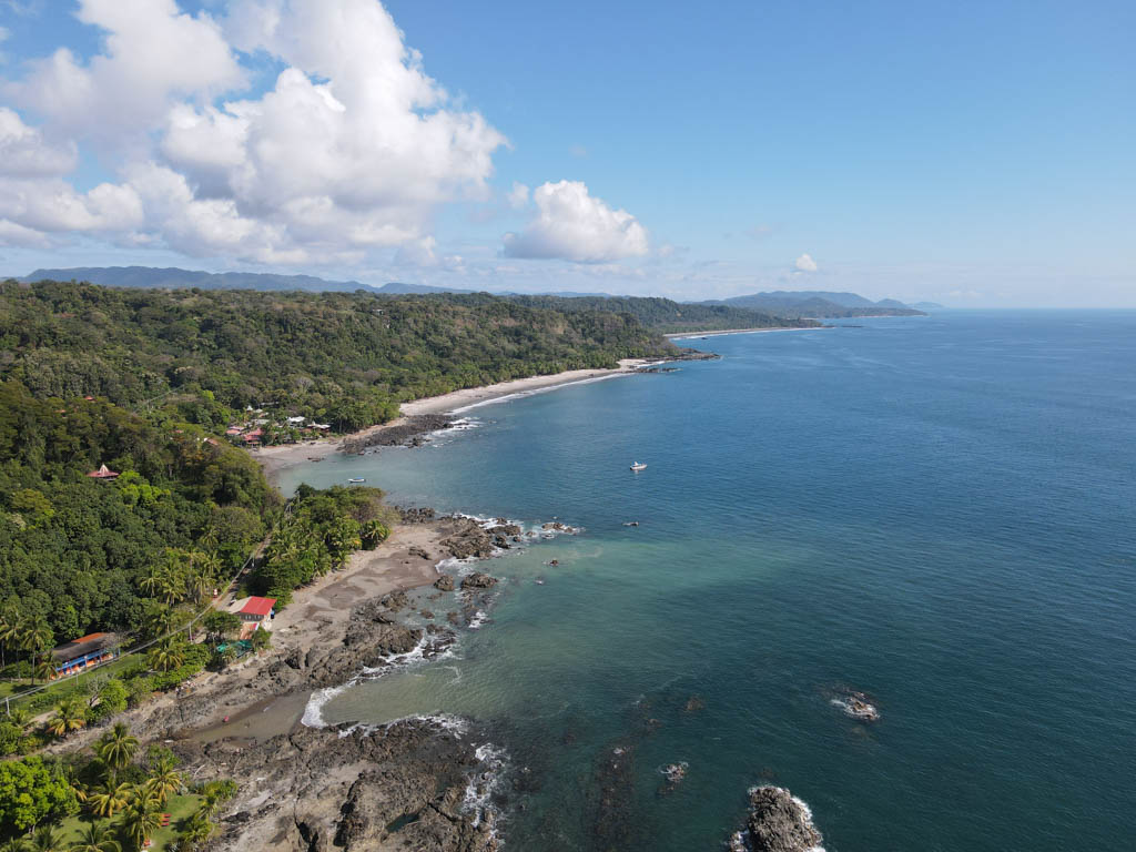 Aerial View of Montezuma, showing the town sandwiched between blue ocean and forest covered hills.