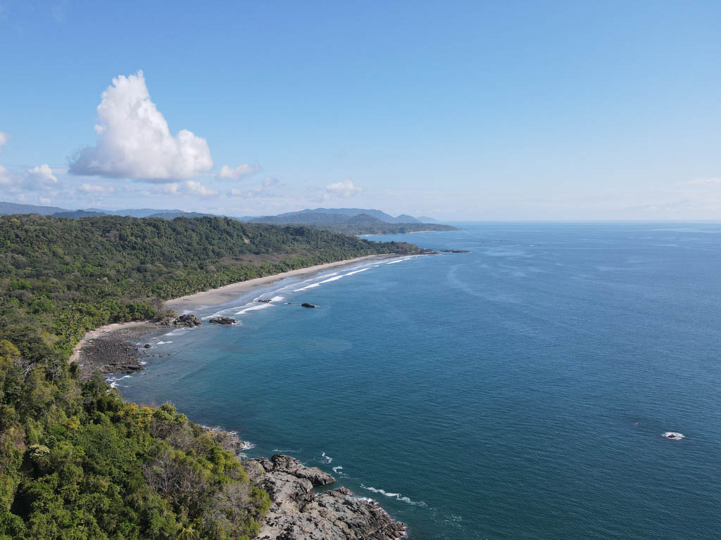 An aerial view of Playa Grande in the distance. Green forest covered hills line along the beaches next to the blue ocean.