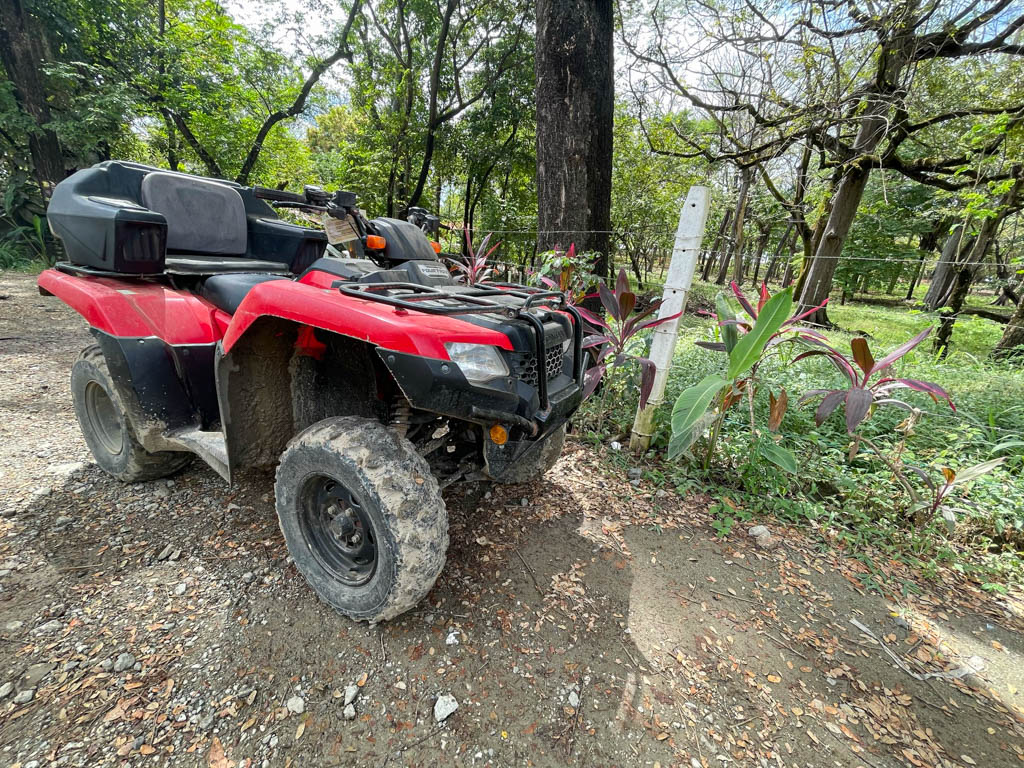 A red and black ATV parked on the road, next to a garden, in Santa Teresa, Costa Rica.
