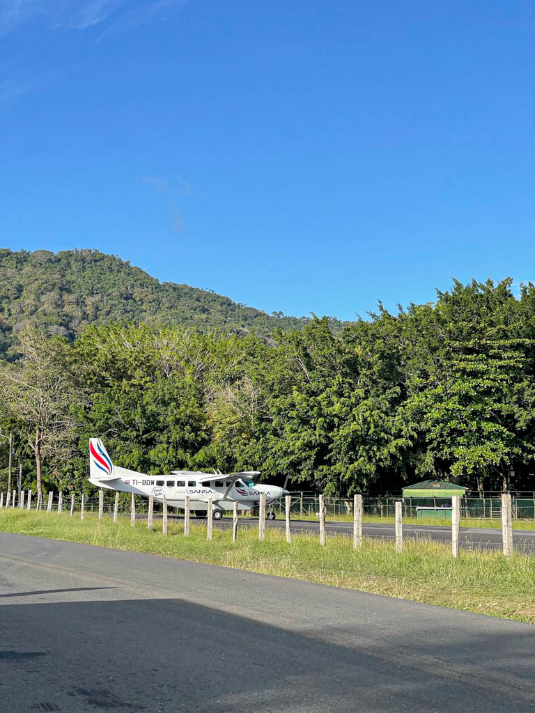 Sansa Air domestic plane, a white colored small aircraft with red and blue design. The plane is ready on the runway at Tambor Airport, Costa Rica.