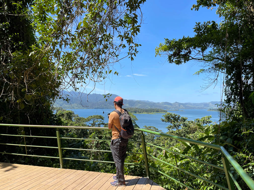 Man standing on viewpoint deck of Peninsula sector. Arenal Lake can be seen from the deck.