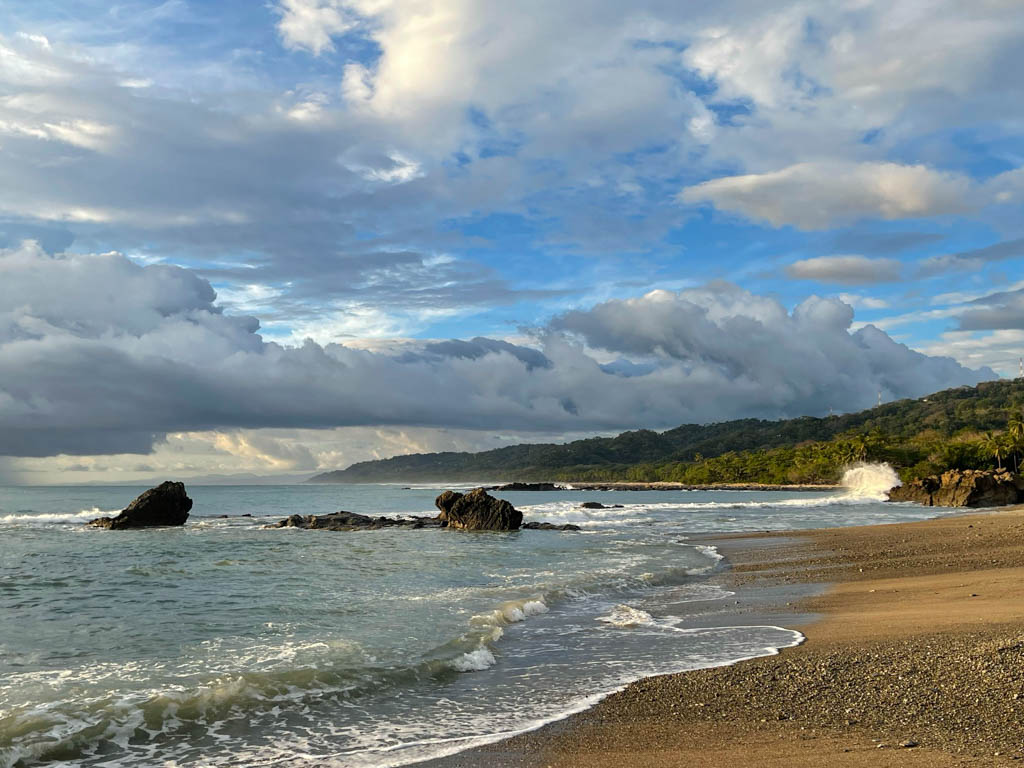 The beach at Malpais Costa Rica. A beautiful yellow sand beach fringed by lush vegetation. White clouds floating in the sky.