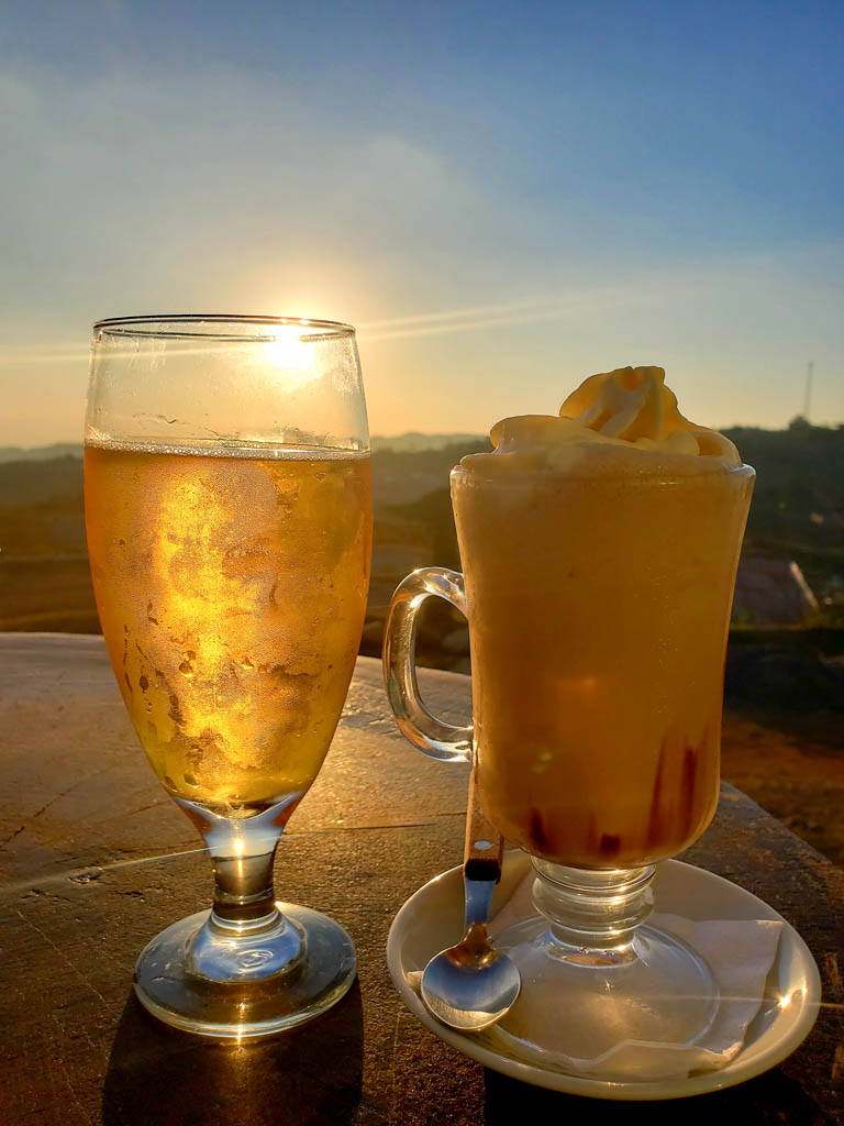 One glass of beer and one glass of cold coffee topped with cream, with sunset view in the background. Location: Morpho's Restaurant, Monteverde.