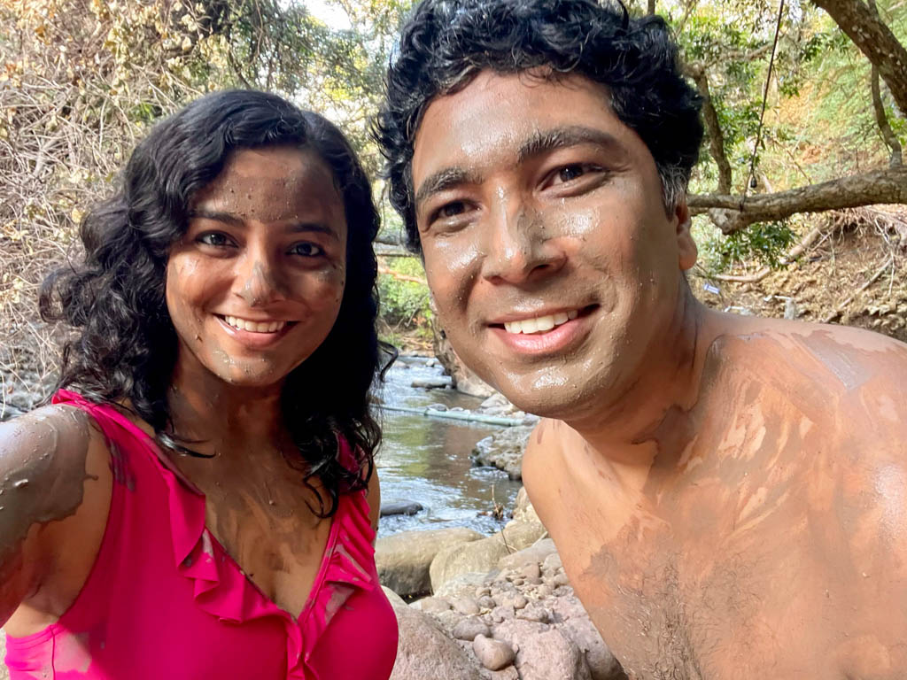 A woman and a man with volcanic mud on their faces and body, getting ready for a volcanic mud bath. Woman is wearing pink swimsuit.