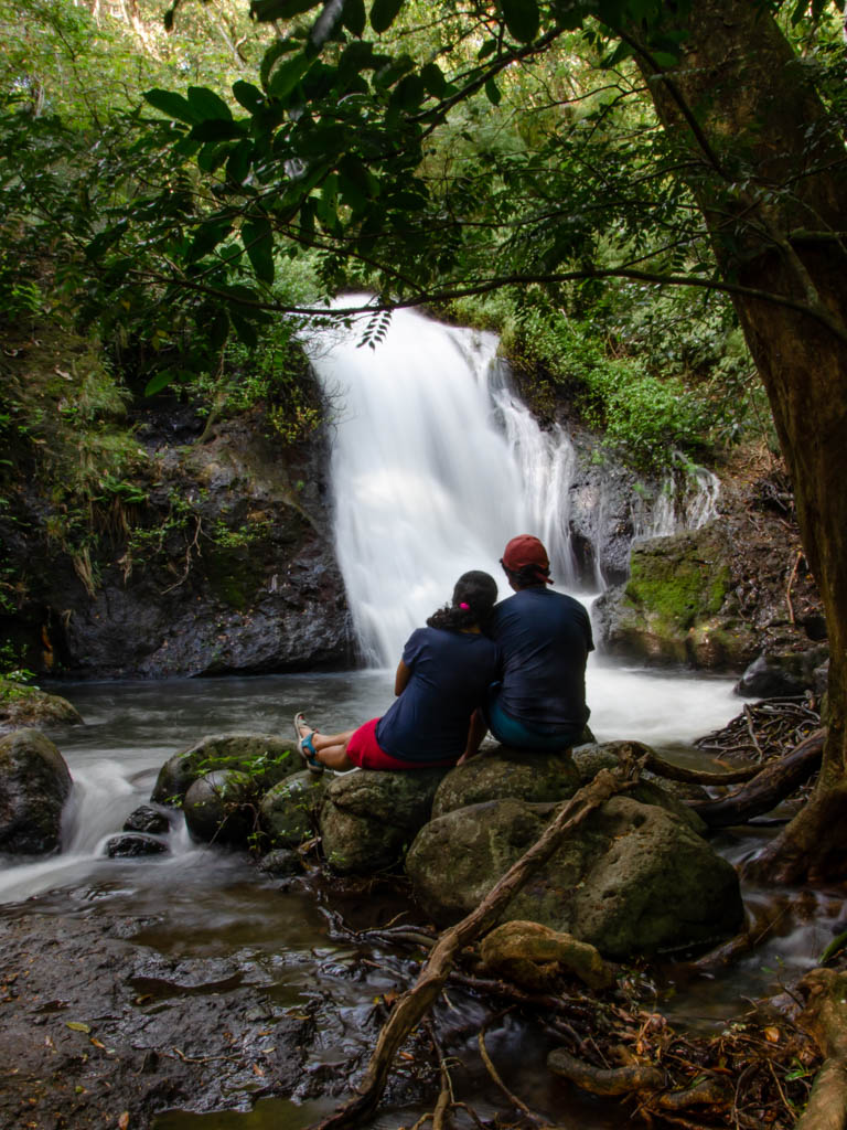 A couple sitting quietly by a waterfall on Rio Negro Waterfalls Trail. Both of them are wearing blue t-shirts.