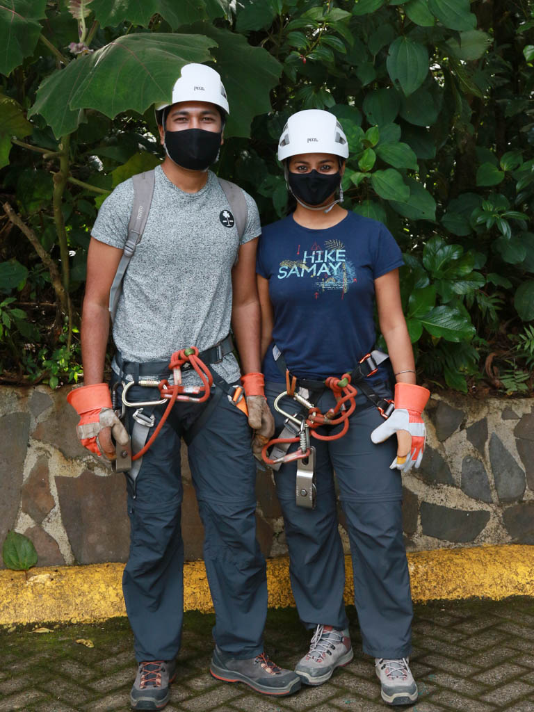 A man and woman with their zip line gears  and mask on.