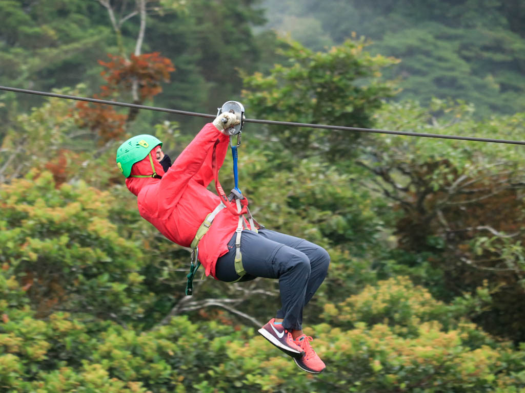 A woman zip-lining in Monteverde, Costa Rica wearing a Rain Jacket which is a packing essential for Costa Rica in the rainy season.
