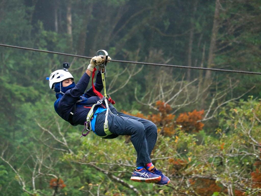 A Man zip lining surrounded by trees with colored leaves.