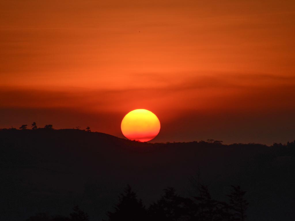 A beautiful sunset view in Monteverde - orange sun setting in the backdrop of a fiery red sky.