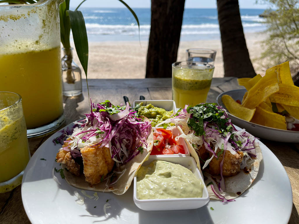 A plate with fish tacos in the main focus, and a bowl of ceviche and passion fruit drinks on the side, served at La Luna restaurant, an oceanfront restaurant at Playa Pelada.