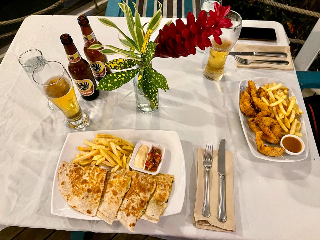 A top view of dining table with beer, shrimp quesadilla and fish fingers. Table is decorated with a vase of flowers.