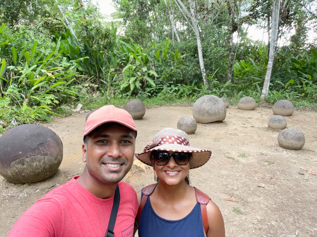 A man and a woman smiling at the camera with the stone spheres behind them.