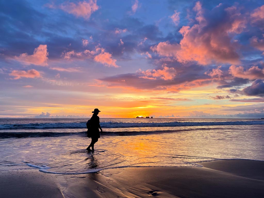 A silhouette of a woman wearing a hat, admiring the sunset colors at Playa Piñuelas in Costa Rica.