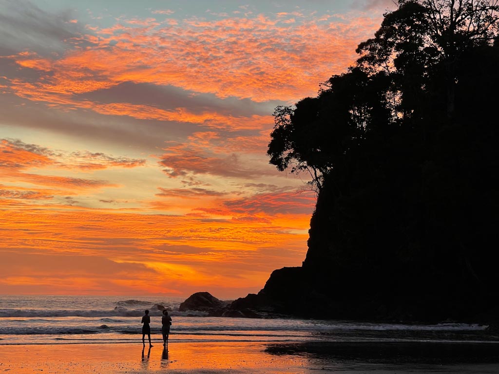 Beach sunset with orange sky and a cliff silhouette in the foreground.