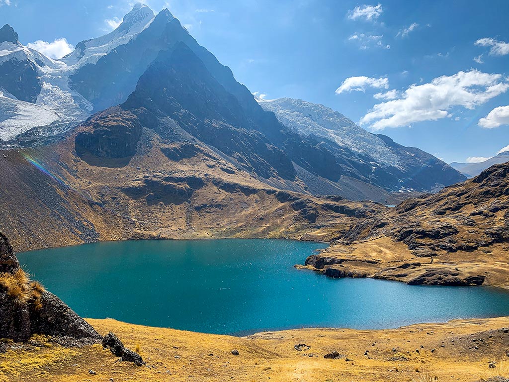 A blue lake surrounded by snowcapped Andes mountains, a stunning sight during the Ausangate trek in Peru.