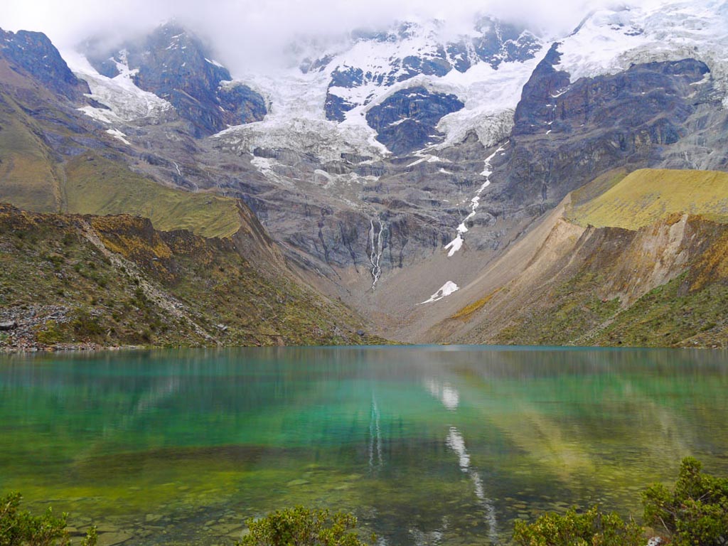 View of an emerald colored lake Humantay, surrounded by snowcapped mountains. Humantay Lake is one of the best places to visit in Peru.
