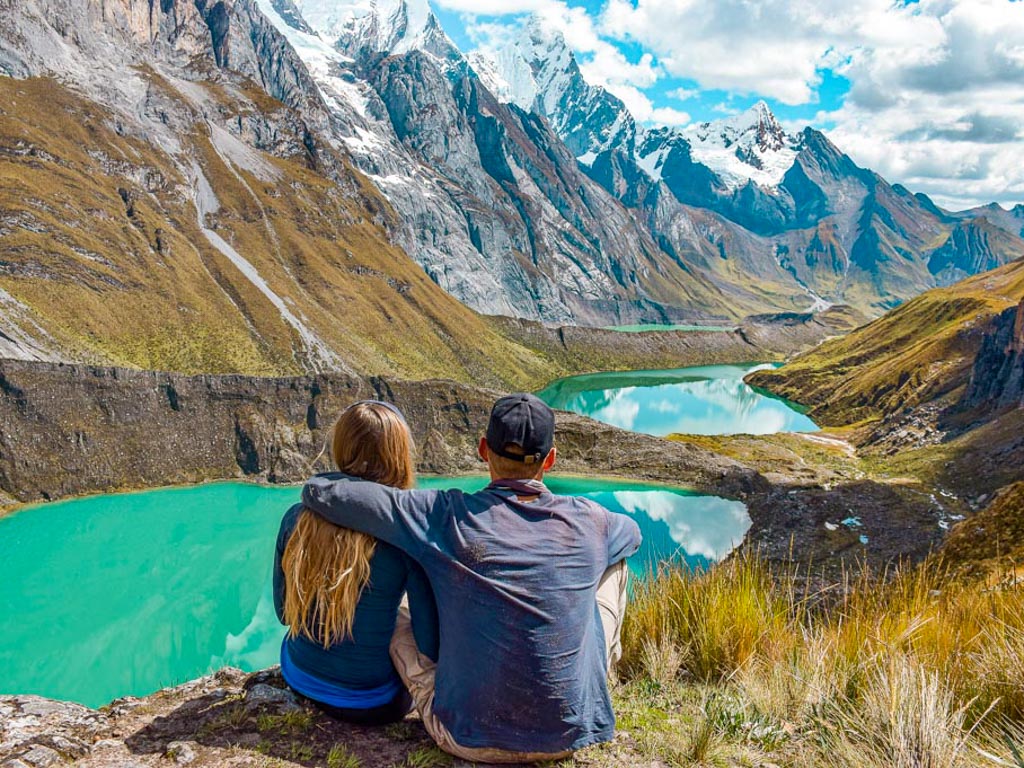 The backside of a man and a woman sitting by the Tres Lagunas in Huayhuash, a treak from Huaraz, one of the best places to visit in Peru.