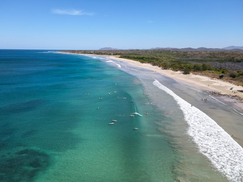 A drone shot of surfers waiting for the wave at Avellanas beach. Surfing is a great activity to include in the Costa Rica itinerary for surfing beginners as well as surfing pros.