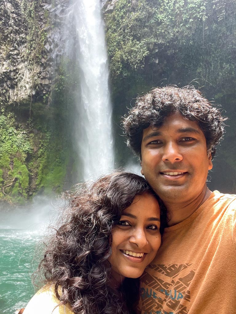 Man and woman smiling at the camera while posing for a selfie at La Fortuna waterfall.
