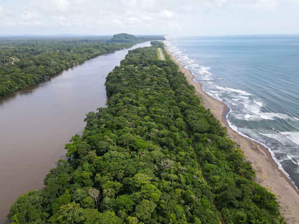 Aerial view of Tortuguero air strip, set amidst lush greenery, with Tortuguero Lagoon on one side and Caribbean Sea on the other.