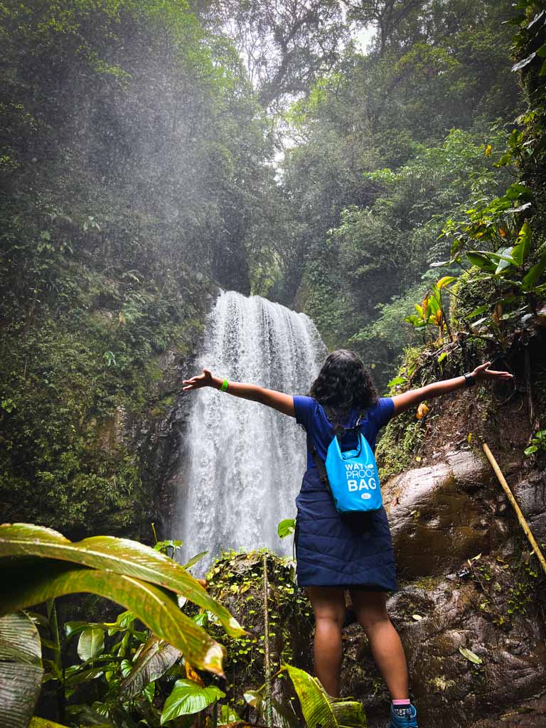 The backside view of a woman enjoying the view of the waterfall in the green jungle.