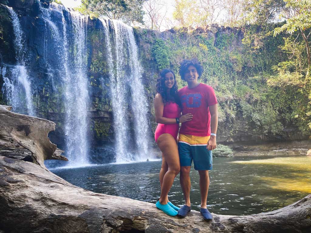 Man and woman in front of Llanos de Cortes waterfall in Guanacaste, Costa Rica. Both of them are wearing water shoes, a must have item on your  Costa Rica packing list.