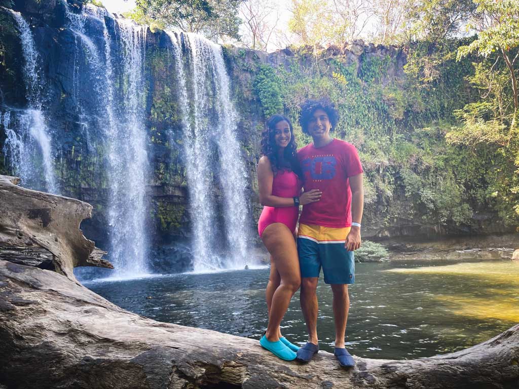 Man and woman in front of Llanos de Cortes waterfall in Guanacaste, Costa Rica. Both of them are wearing water shoes, a must have item on your  Costa Rica packing list.