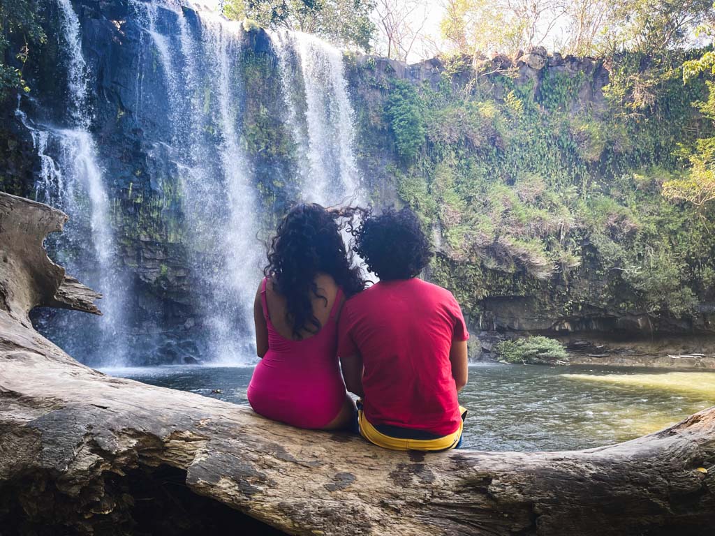 A couple seated on a tree log, enjoying the views of Llanos del Cortes waterfall.