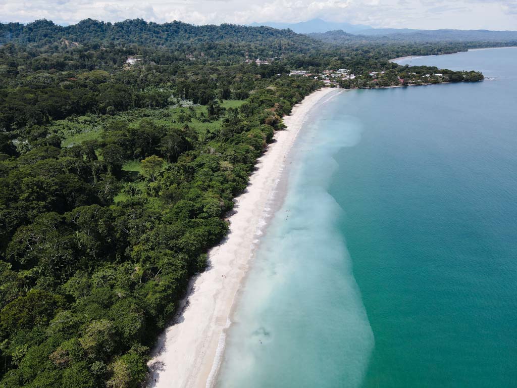 Aerial view of lush tropical forest lining the Caribbean Sea, at Cahuita National Park, with the Cahuita town situated at the end of the National Park.