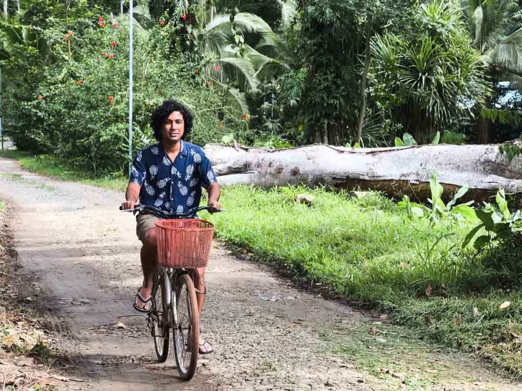 A man wearing deep blue floral shirt and shorts, riding a bicycle near Playa Negra in Caribbean Costa Rica.